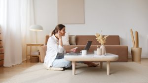 A woman sits on the floor of her living room, inserting wireless earbuds